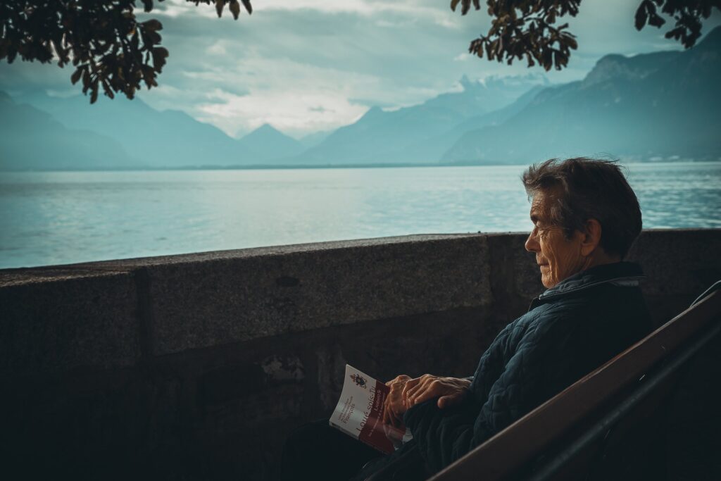 Old man sitted by the lake with a book in his hand